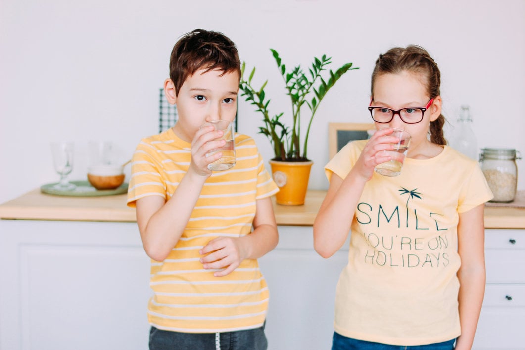 Smiling boy and girl drink clean water at home