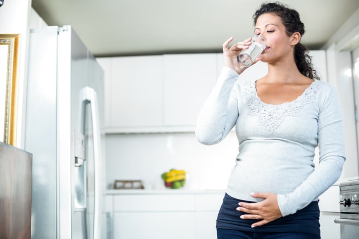 pregnant woman drinking water from refrigerator