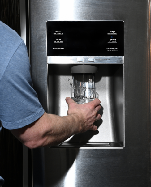 A person filling up a glass of water from the fridge.